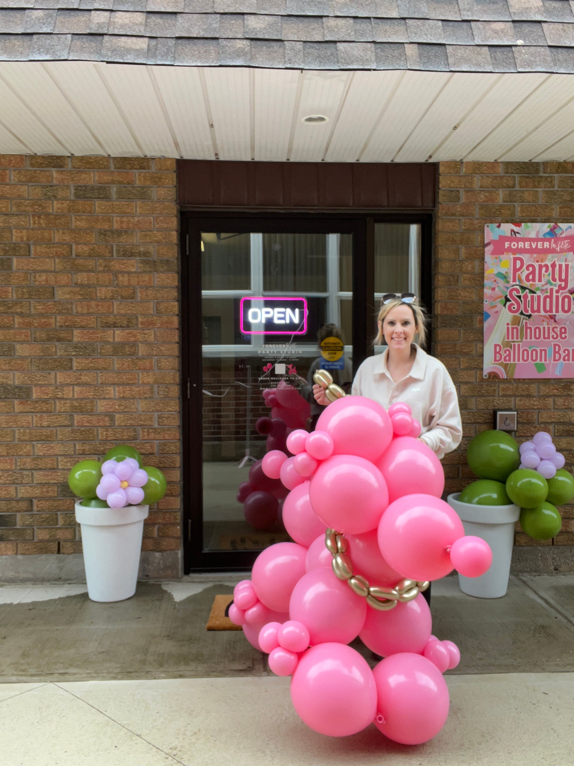 A person standing behind a large, pink balloon sculpture shaped like a dog. The sculpture is designed for use as a decorative item at a party or event.
